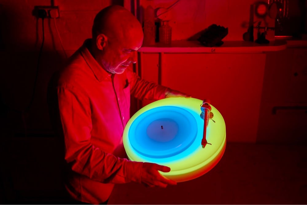 Brian Eno holding his glowing turntable in a dark room