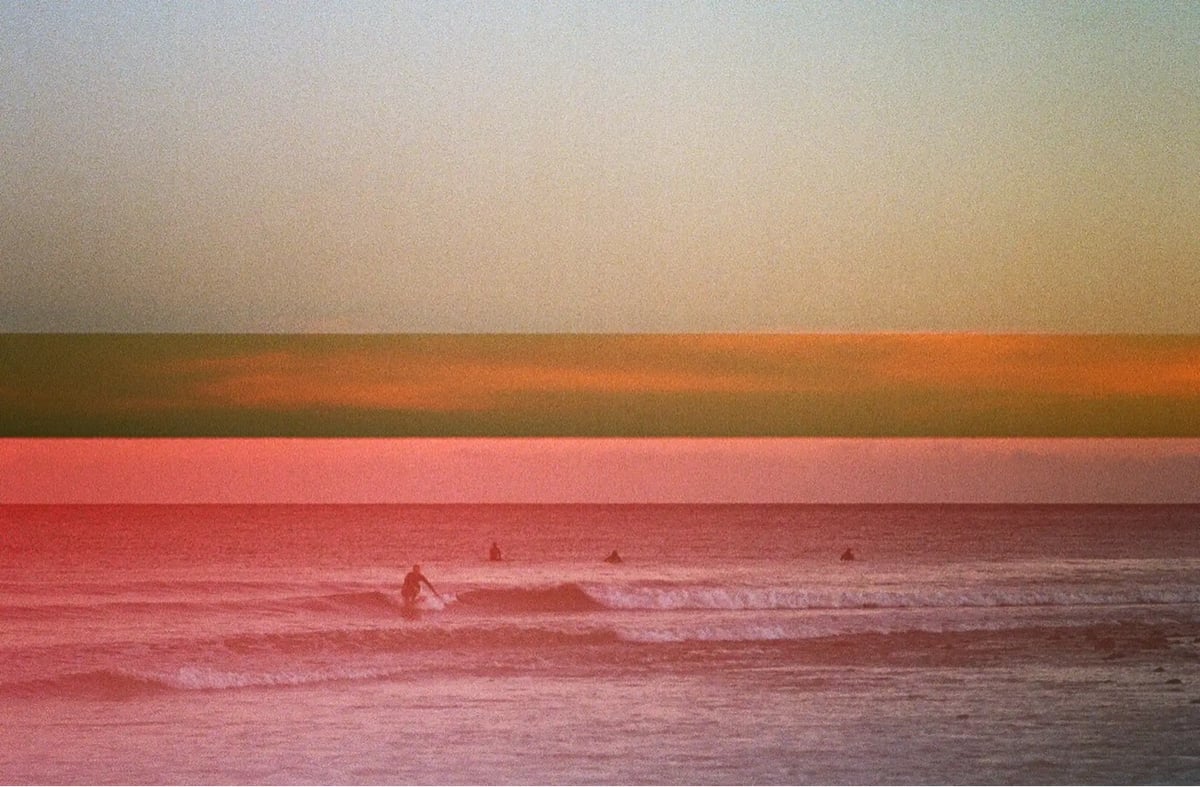 photo of surfers in waves, with a reddish hue