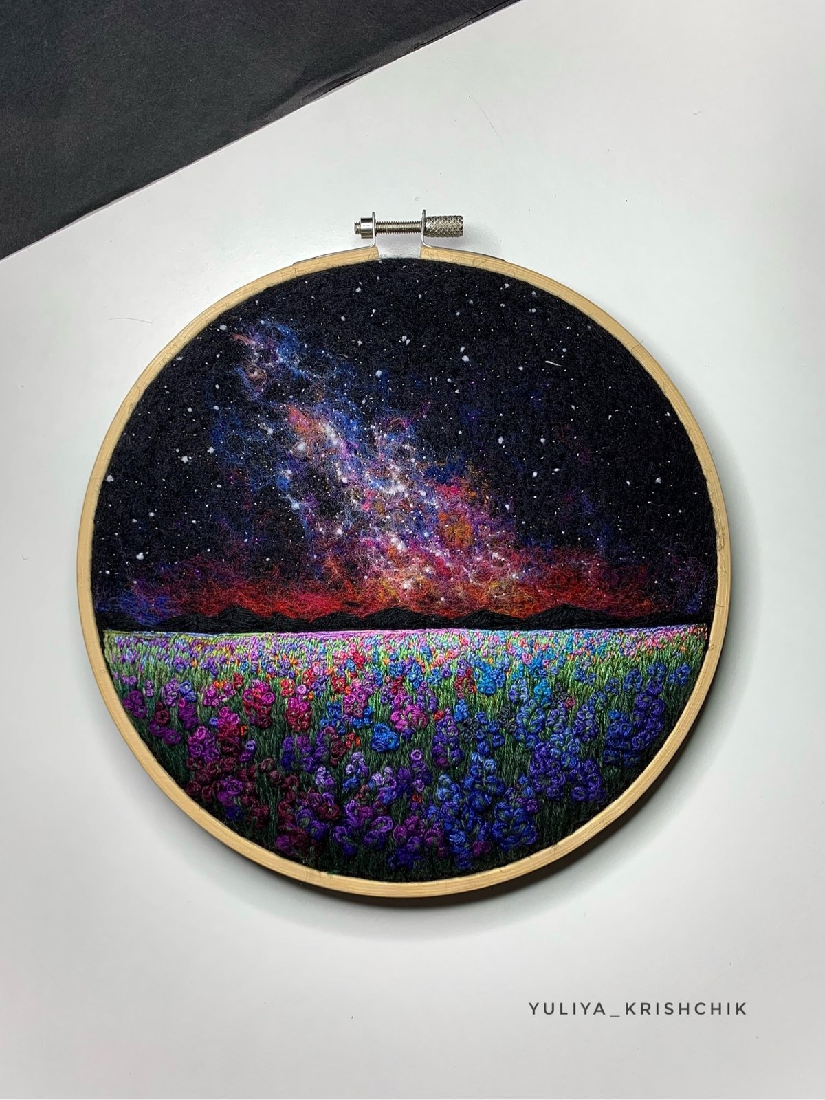 an embroidery piece of the Milky Way above a flowery meadow