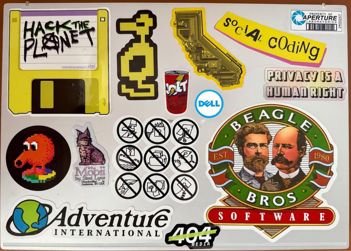 Laptopstickercollectie met gaming- en technische referenties, waaronder Pac-Man, pixelkunst, Aperture Science, Dell en verschillende programmeergerelateerde stickers.