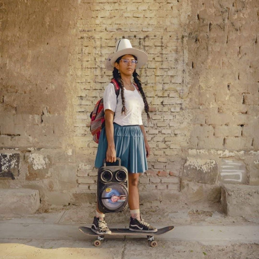 a Bolivian woman in traditional dress stands on a skateboard
