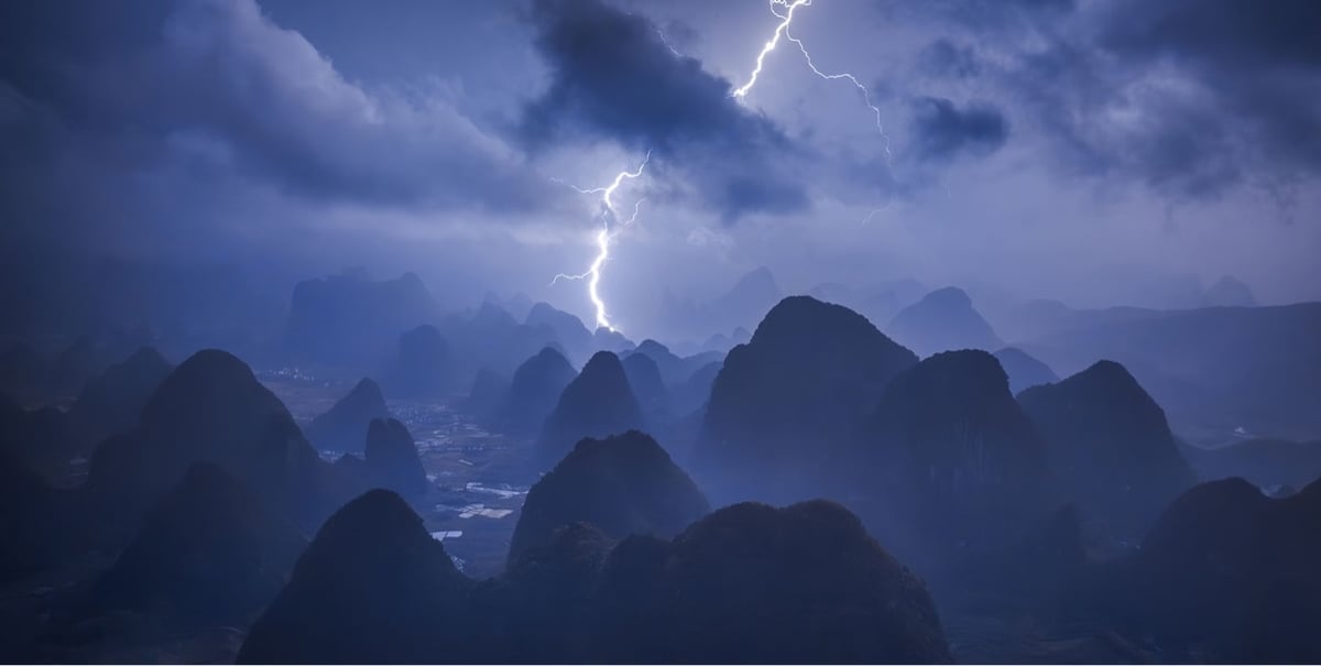 a lightning strike illuminates a mountainous landscape