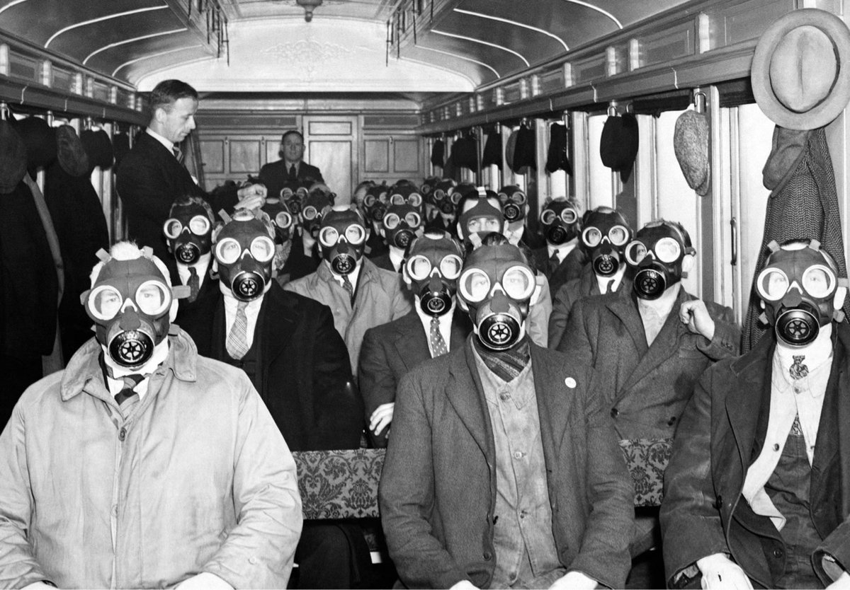 a black & white photo of a bunch of men sitting on a train wearing gas masks
