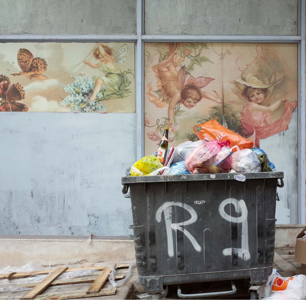 photo of a mural with an angel that looks like it's picking something out of a garbage bin the foreground