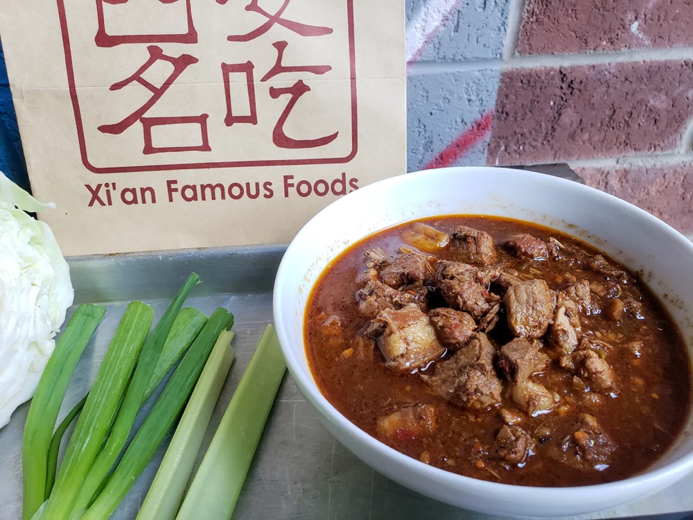 a bowl of stewed meat next to a bunch of scallions
