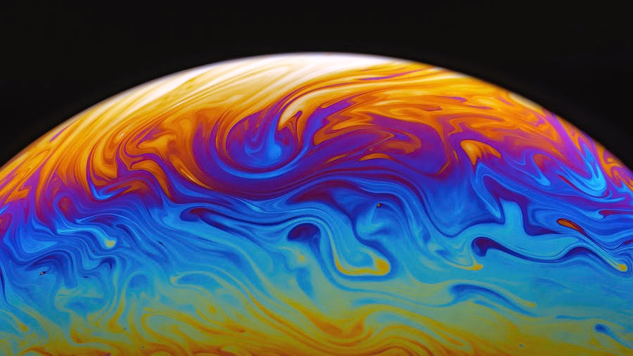 the swirling rainbow surface of a soap bubble from close-up looks like a small planet