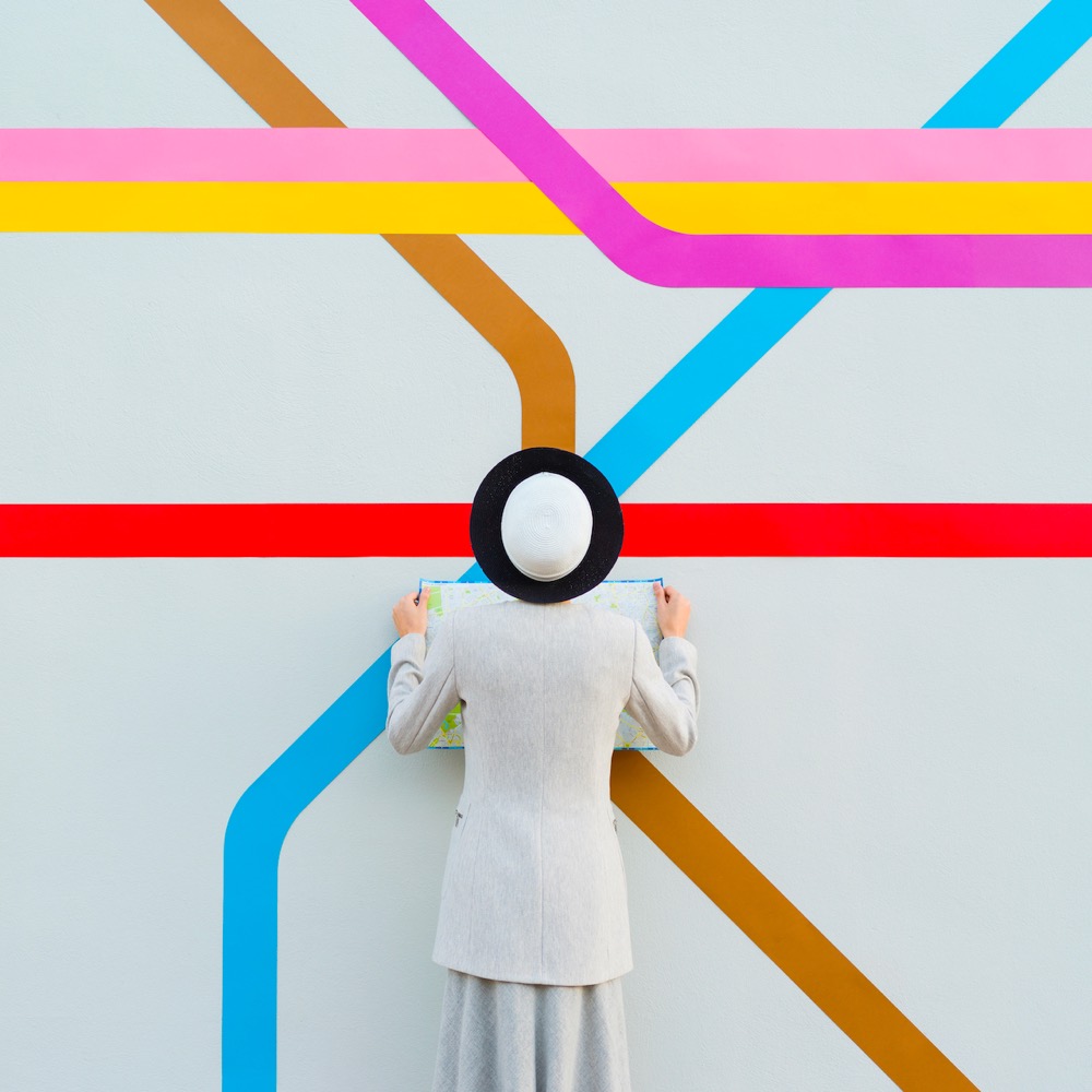 a woman stands in front of a large subway map and her hat appears to be a station