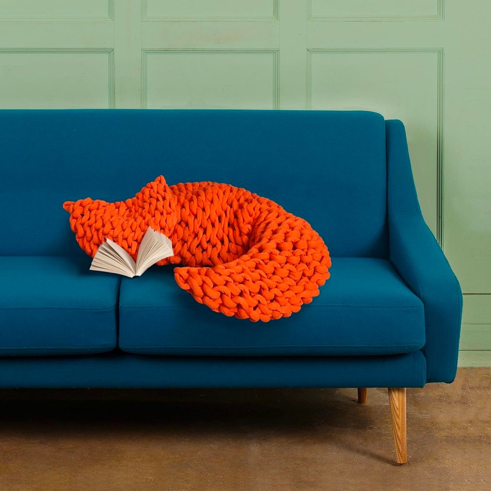 an orange blanket and a book arranged on a sofa to look like a fox