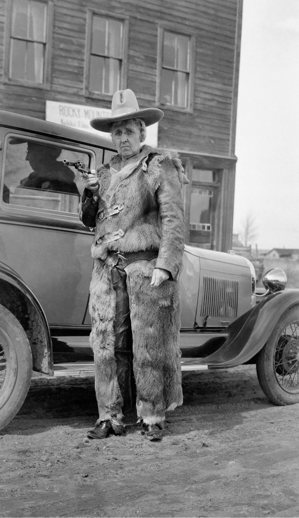 a woman stands in front of a car wearing a deerskin suit