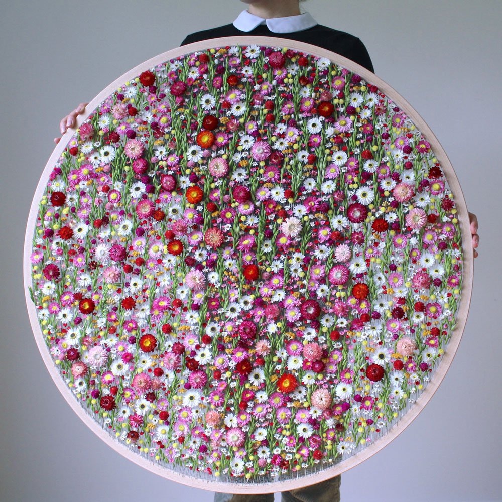 a person holding a huge embroidery decorated with dried flowers