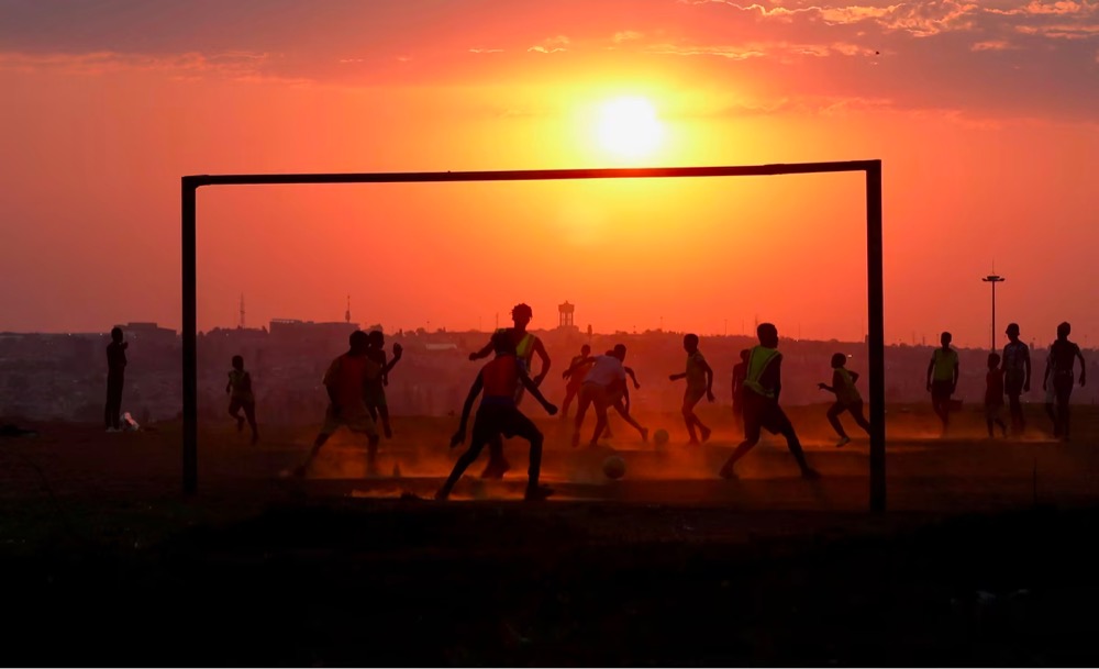 a group of kids play soccer in front of a setting sun