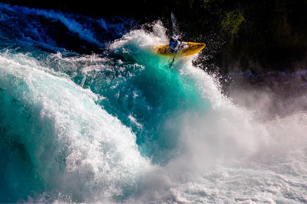 a person in a kayak shoots out of a massive wave in the rapids