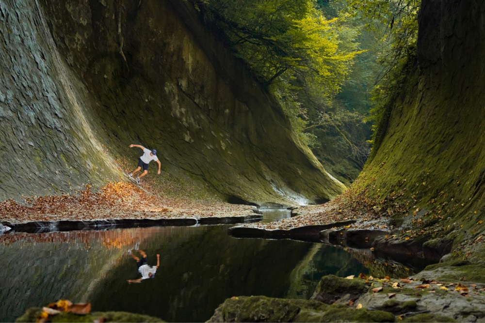 a man skateboards on a curved rock face next to a stream in the forest