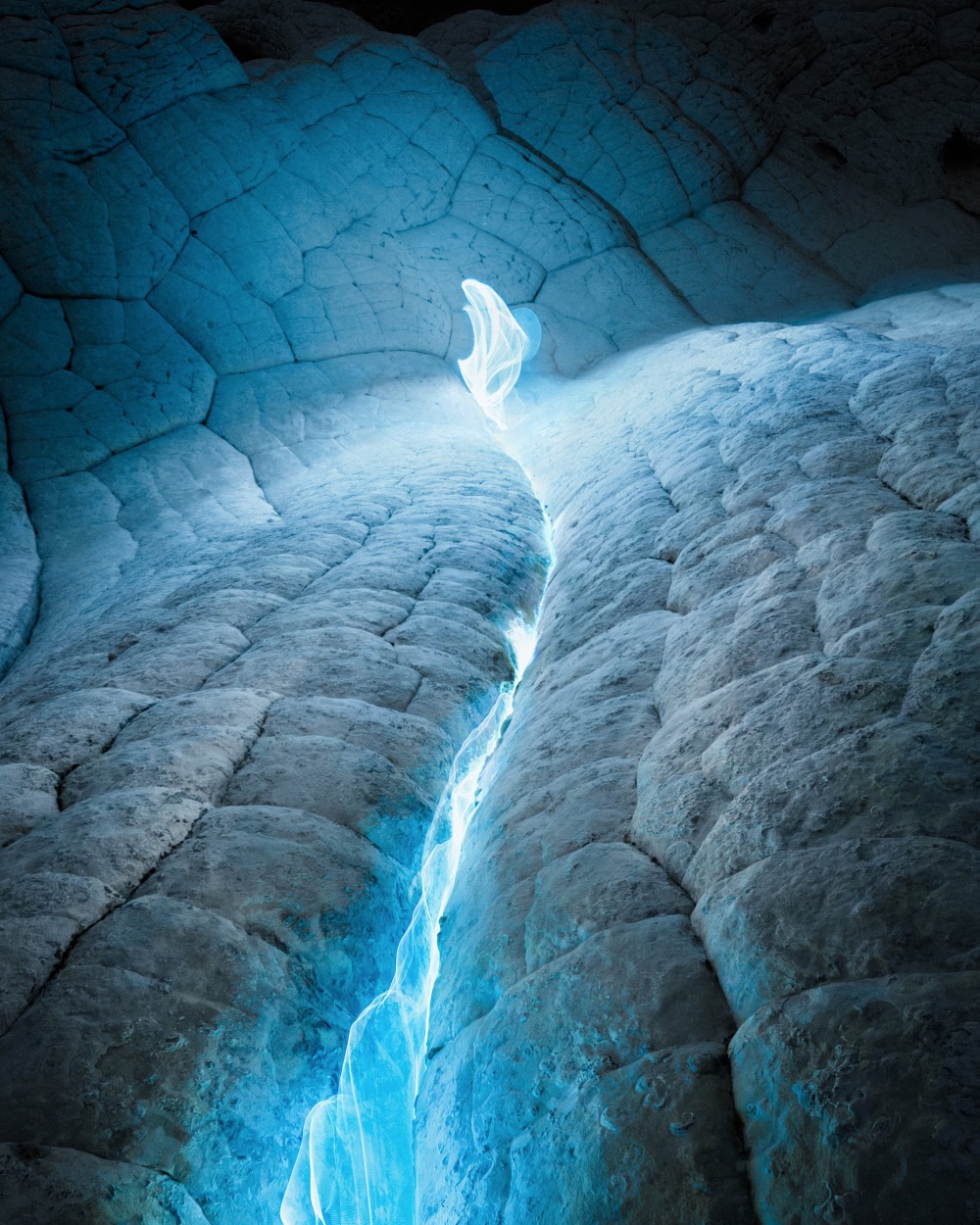 a blue shft of light glows in a rocky crack
