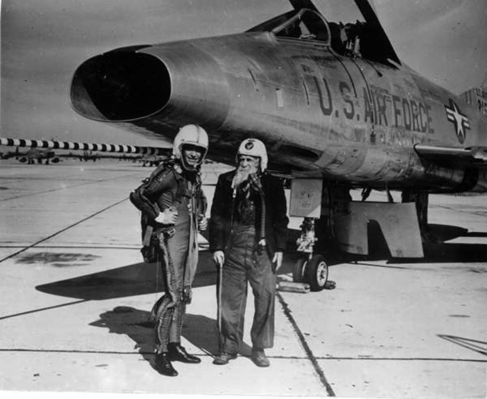 two men standing in front of a fighter jet